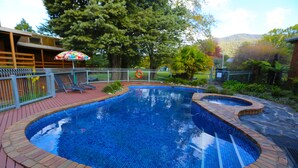 Una piscina con borde de azulejos, rodeada por un patio de ladrillos y una valla de metal.