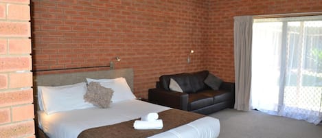 Habitación de hotel con pared de ladrillo, cama con sábanas blancas, sofá de cuero negro y una ventana grande con cortinas.