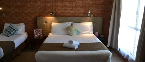 A hotel room with two beds, a brick wall, and a window with curtains.