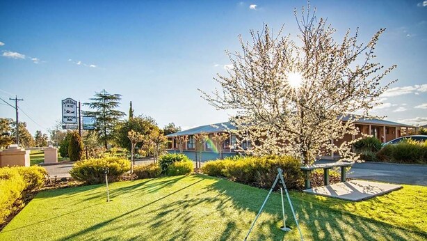 Un campo de golf con un putting green, un árbol y un edificio al fondo.