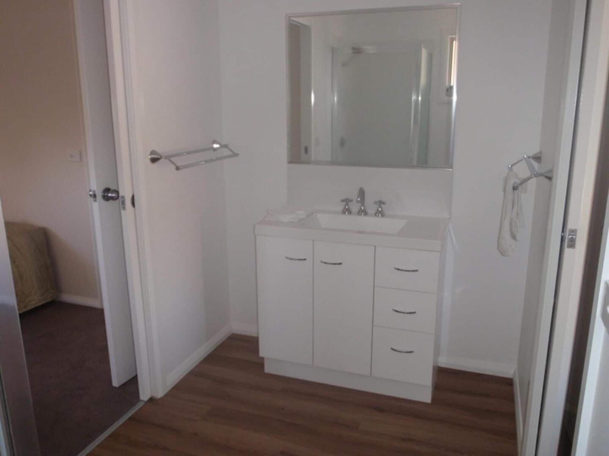 A small, clean bathroom with a white vanity, a mirror, and a towel rack.