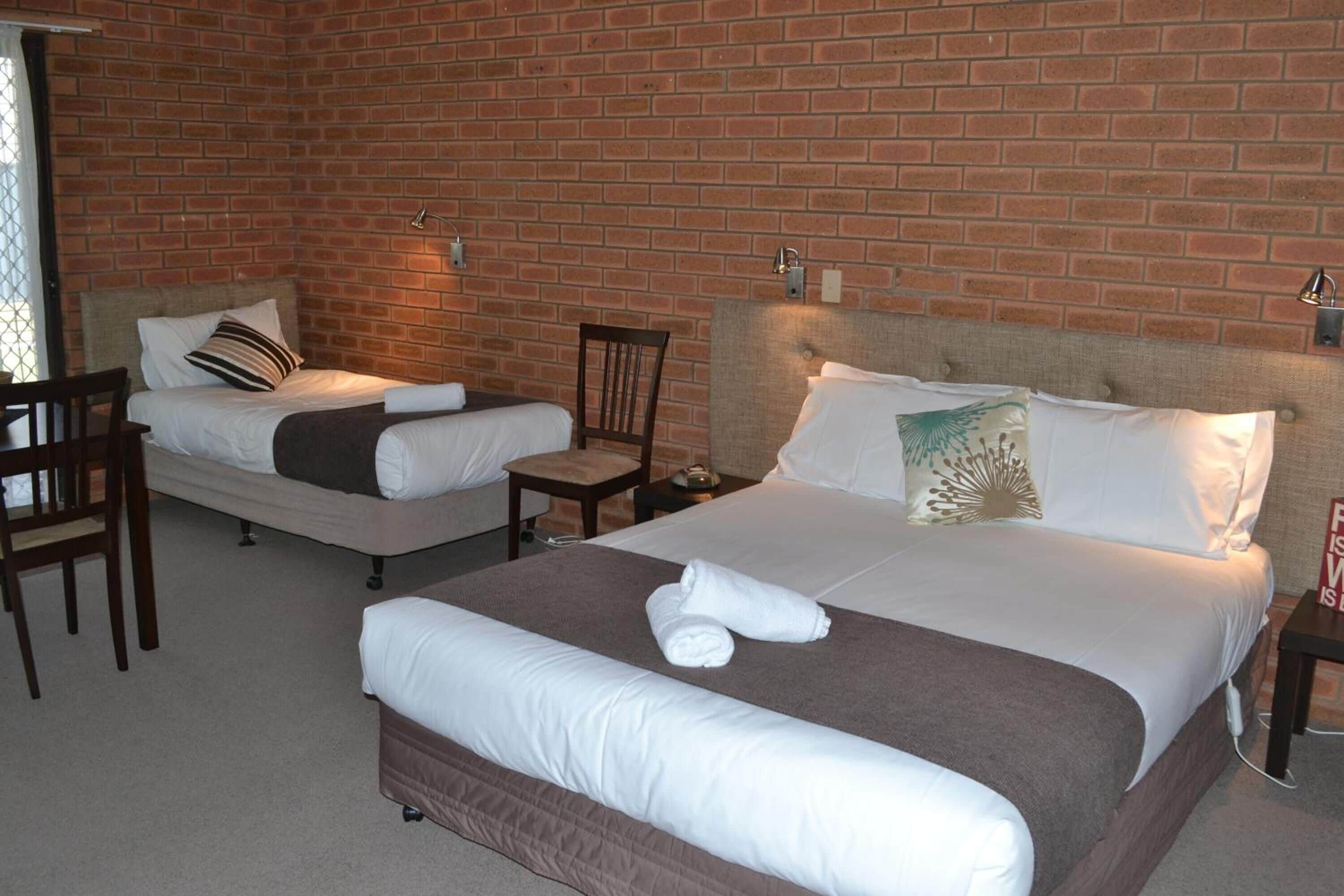 Habitación de hotel con dos camas, un muro de ladrillo y una pequeña mesa con una silla.