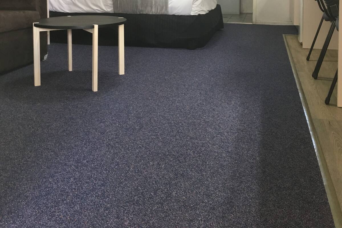 Ein kleiner Raum mit Bett, Tisch, Stuhl, Topfpflanze und Spiegel.