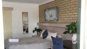 A bedroom with a bed, a desk, a chair, a potted plant, and a wall-mounted artwork. - The Jolly Swagman Motor Inn (Goondiwindi)
