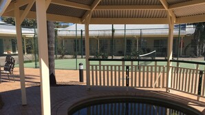 A covered outdoor area with a pool, brick flooring, and a fenced tennis court in the background. - The Jolly Swagman Motor Inn (Goondiwindi)