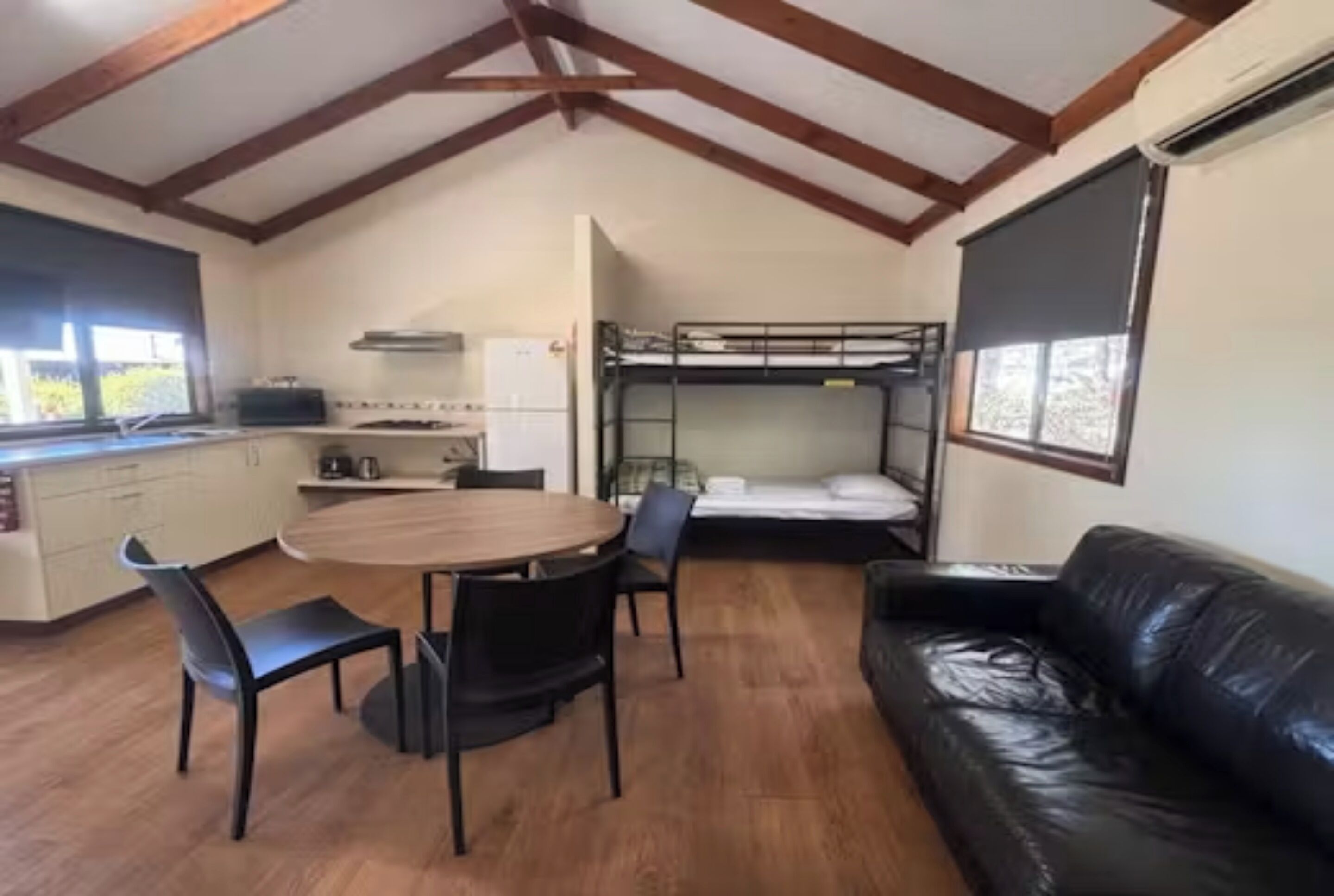 Une pièce compacte comprenant un lit superposé, une table à manger avec des chaises, un canapé en cuir et un coin cuisine.