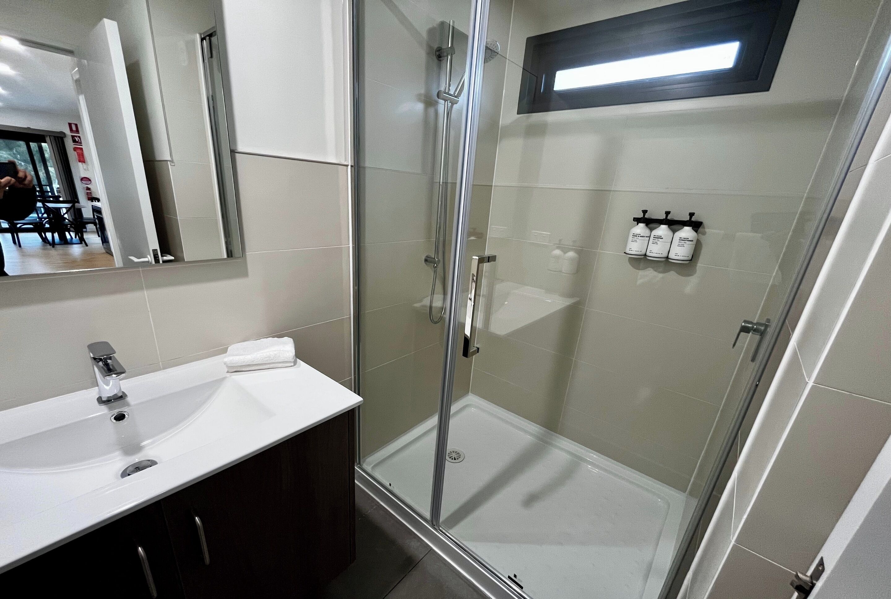 Un baño moderno con ducha de vidrio, un lavamanos blanco y un espejo sobre él.
