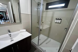 Un baño moderno con ducha de vidrio, un lavamanos blanco y un espejo sobre él.