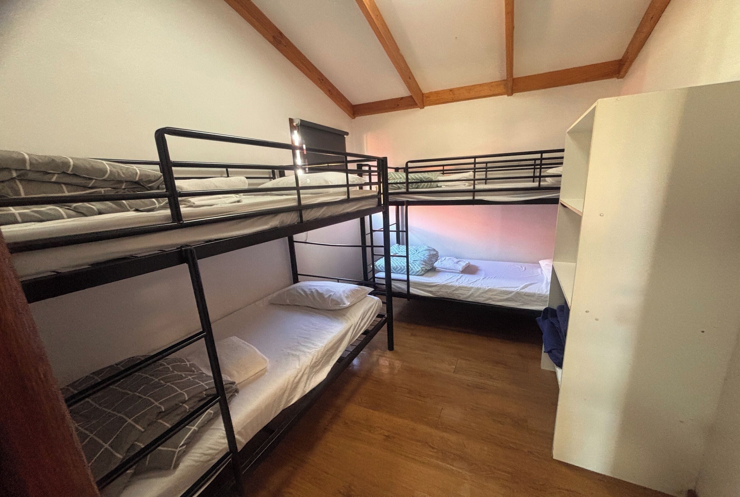 A room with bunk beds, wooden flooring, and a white wall.