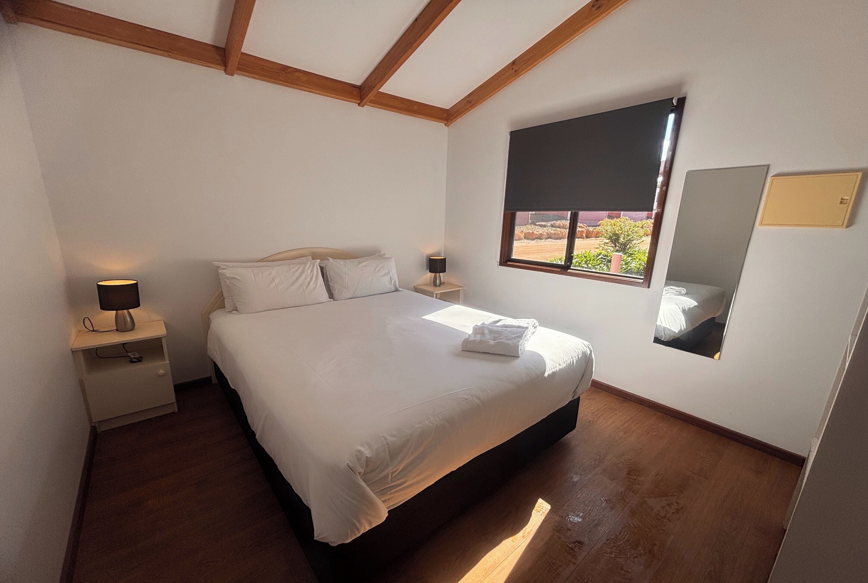 Un dormitorio con cama, mesitas de noche, ventana con vistas y un espejo en la pared.