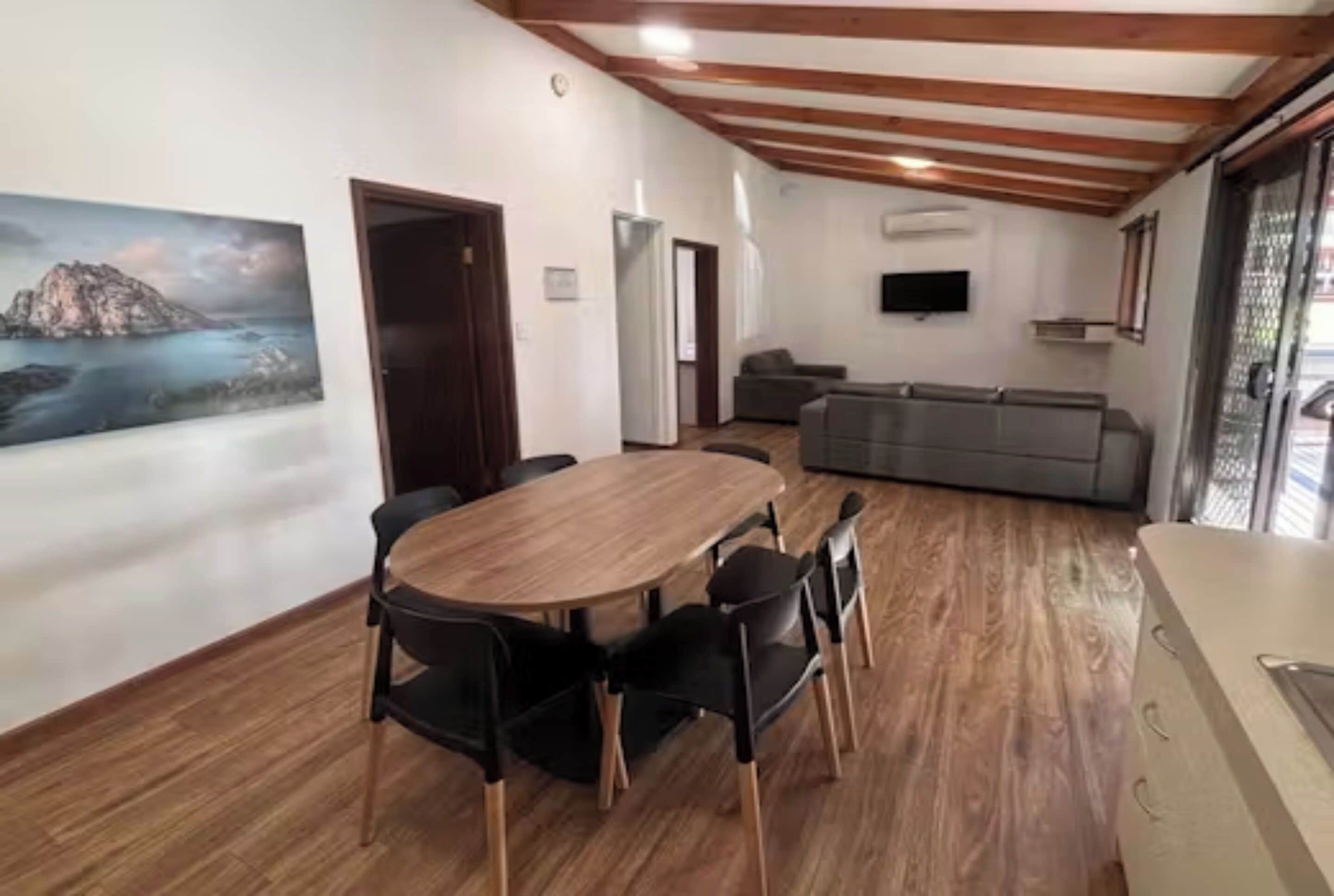 Un comedor con una mesa y sillas de madera, un cuadro en la pared y un sofá al fondo.
