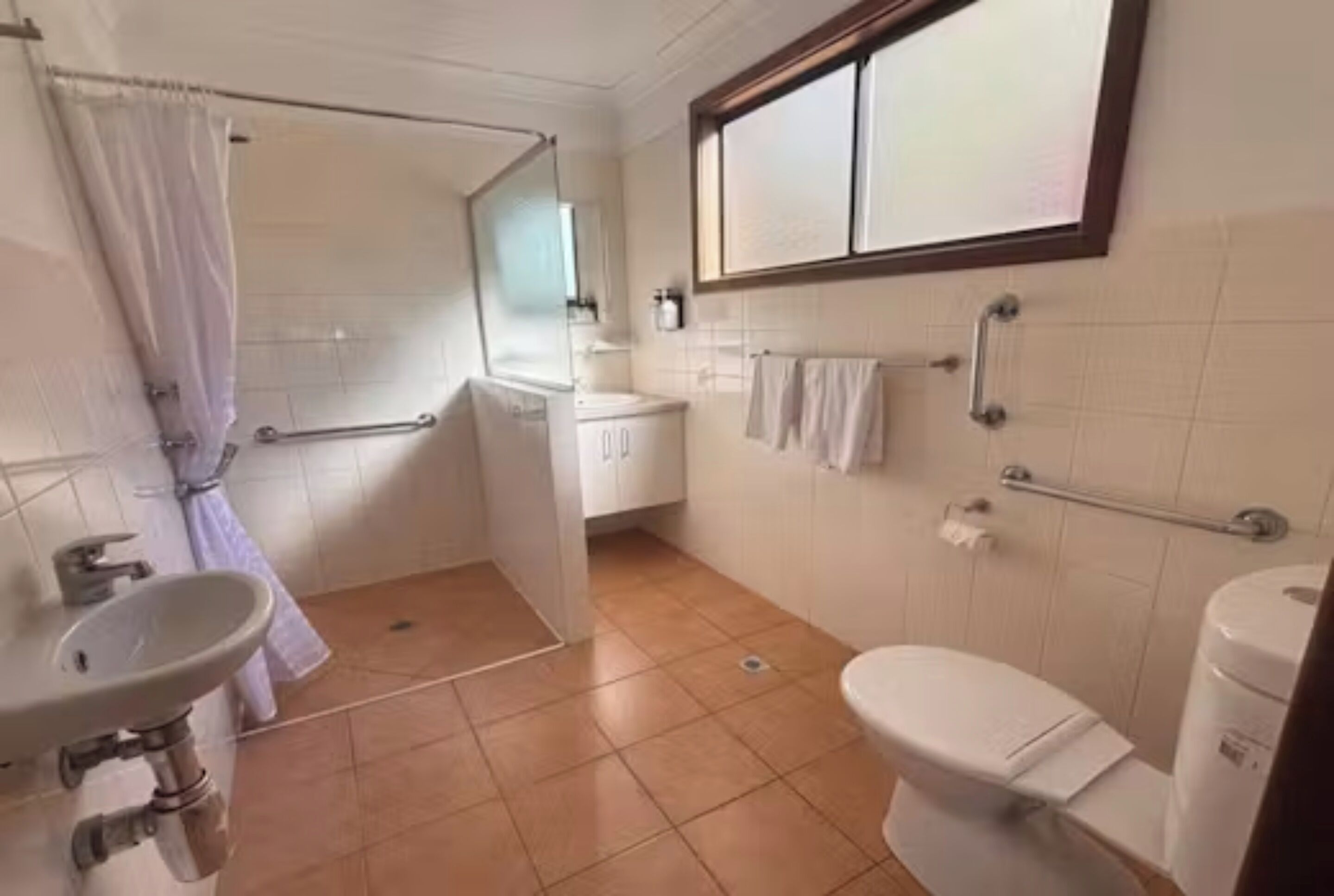 A bathroom with a shower, toilet, sink, and a window above the sink.