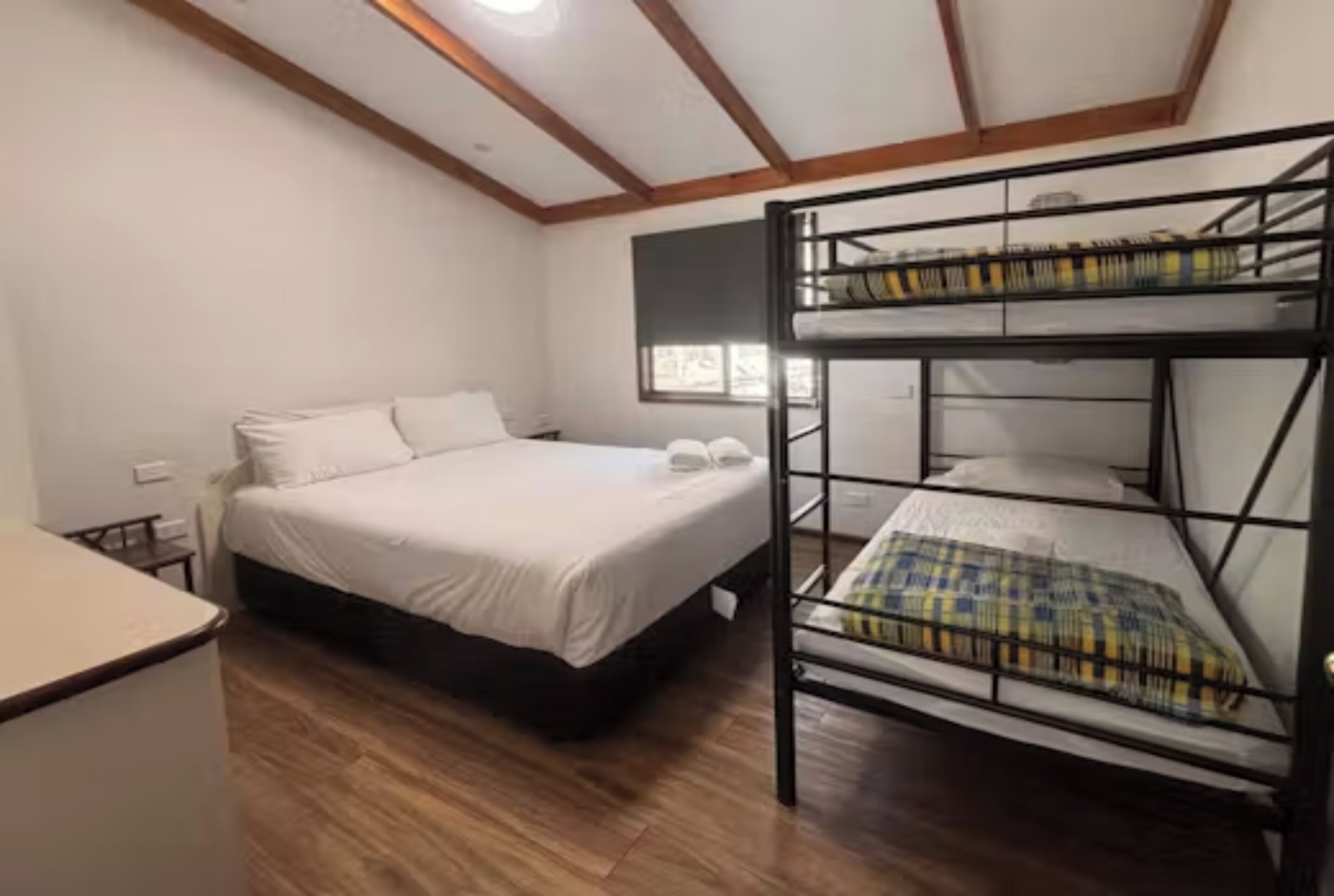 Een kamer met een stapelbed, een enkel bed, houten vloeren en een raam.