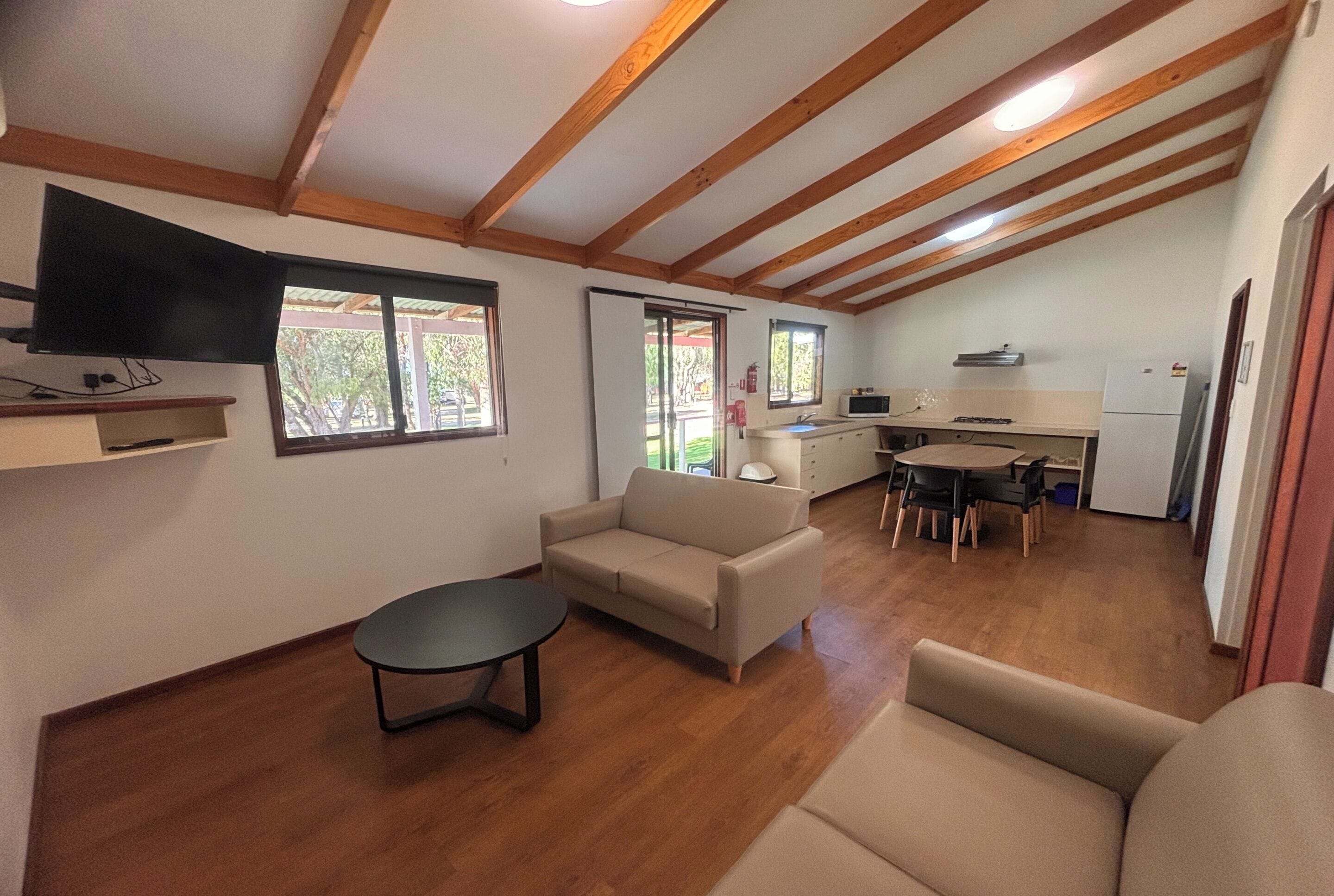 Un espacio habitable compacto con sofá, una mesita, kitchenette y televisor montado en la pared.