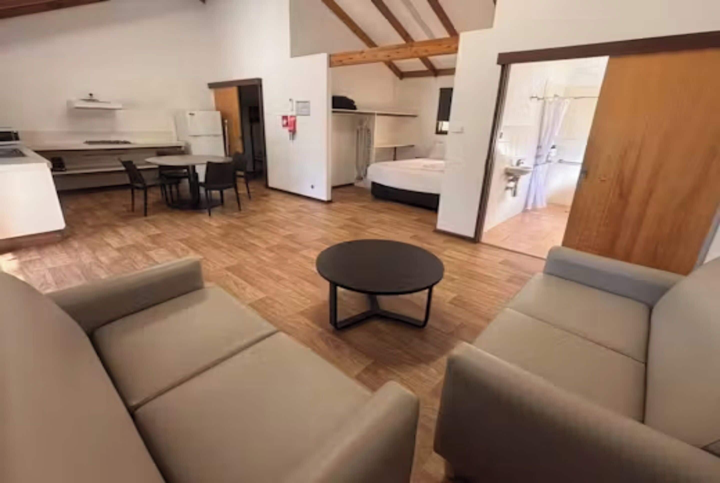Habitació amb sofà, taula rodona petita, llit i zona de cuina compacta.