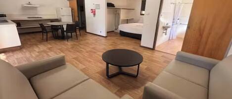 A room with a sofa, a small round table, a bed, and a kitchenette area.