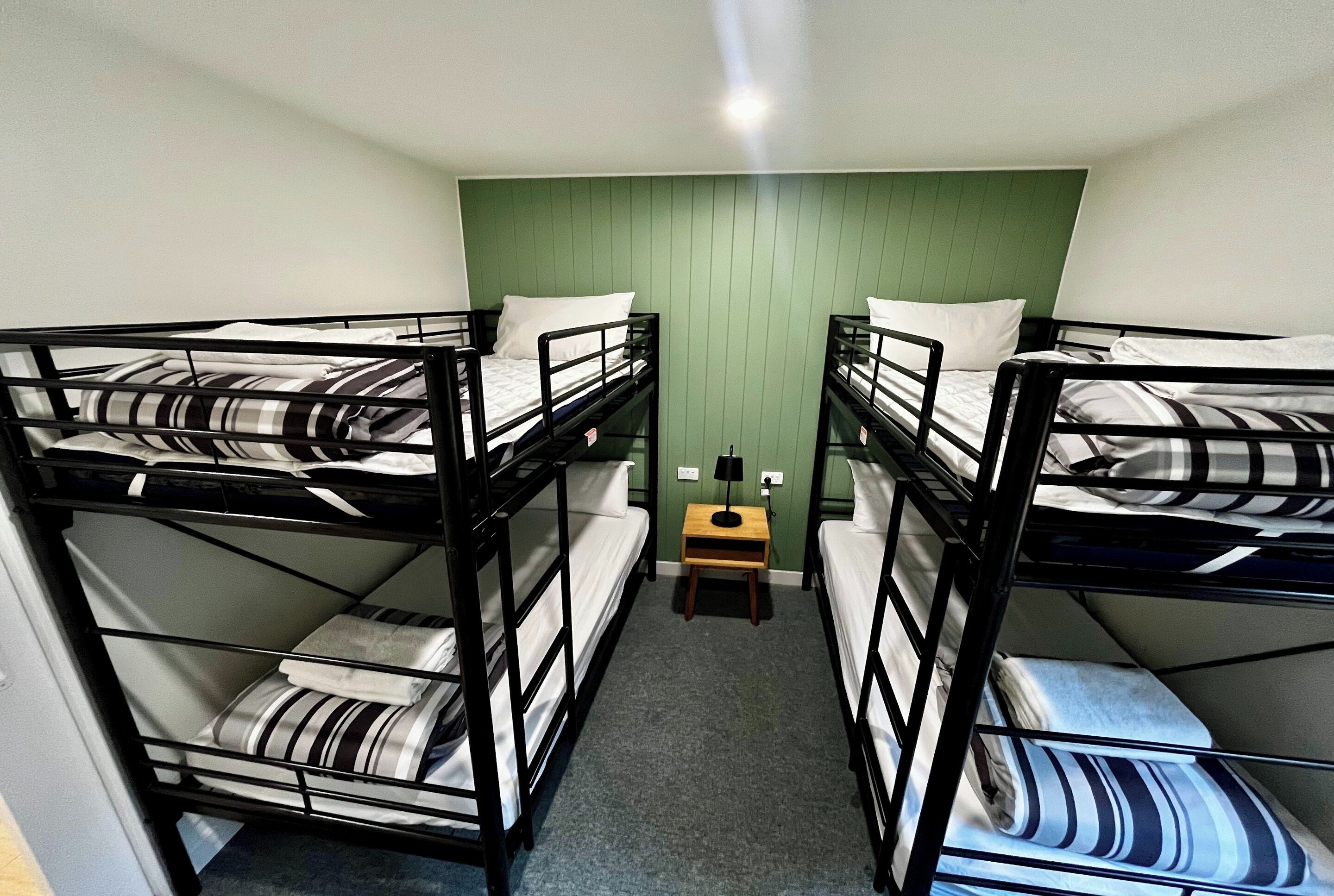 Una habitación con literas, una mesita de noche de madera y una pared verde.