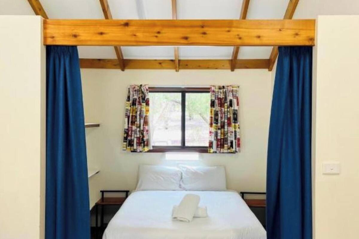 Een slaapkamer met een houten plafond, een bed met wit beddengoed en blauwe gordijnen.