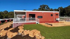 Un bâtiment moderne de couleur rouge, doté d’un balcon blanc, entouré d’une pelouse bien entretenue et d’arbres.