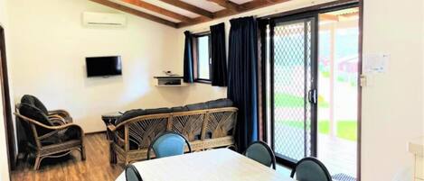 A room with a dining table, chairs, a sofa, a TV, and a sliding glass door leading to an outdoor area.