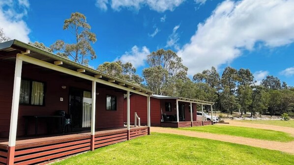 A row of red cabins with wooden decks and a clear blue sky. - Discovery Parks - Margaret River (Metricup)