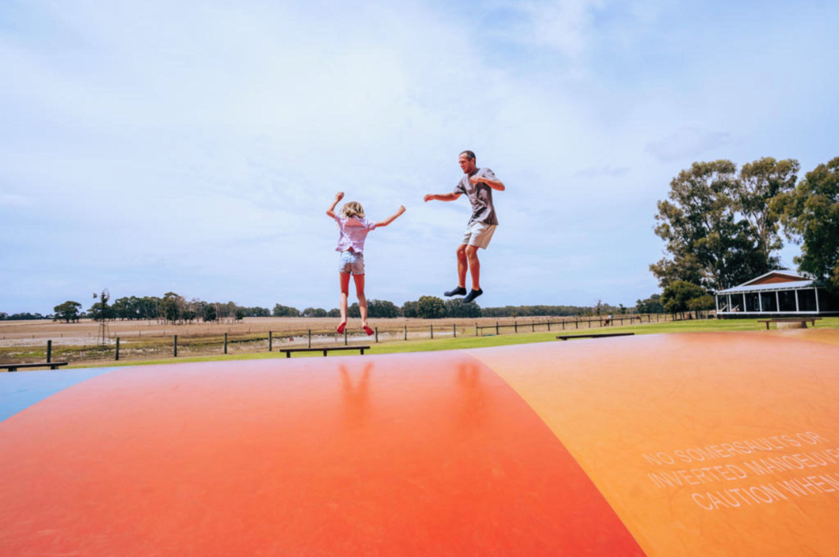 A man and a child jumping on a colorful outdoor platform with a warning sign.