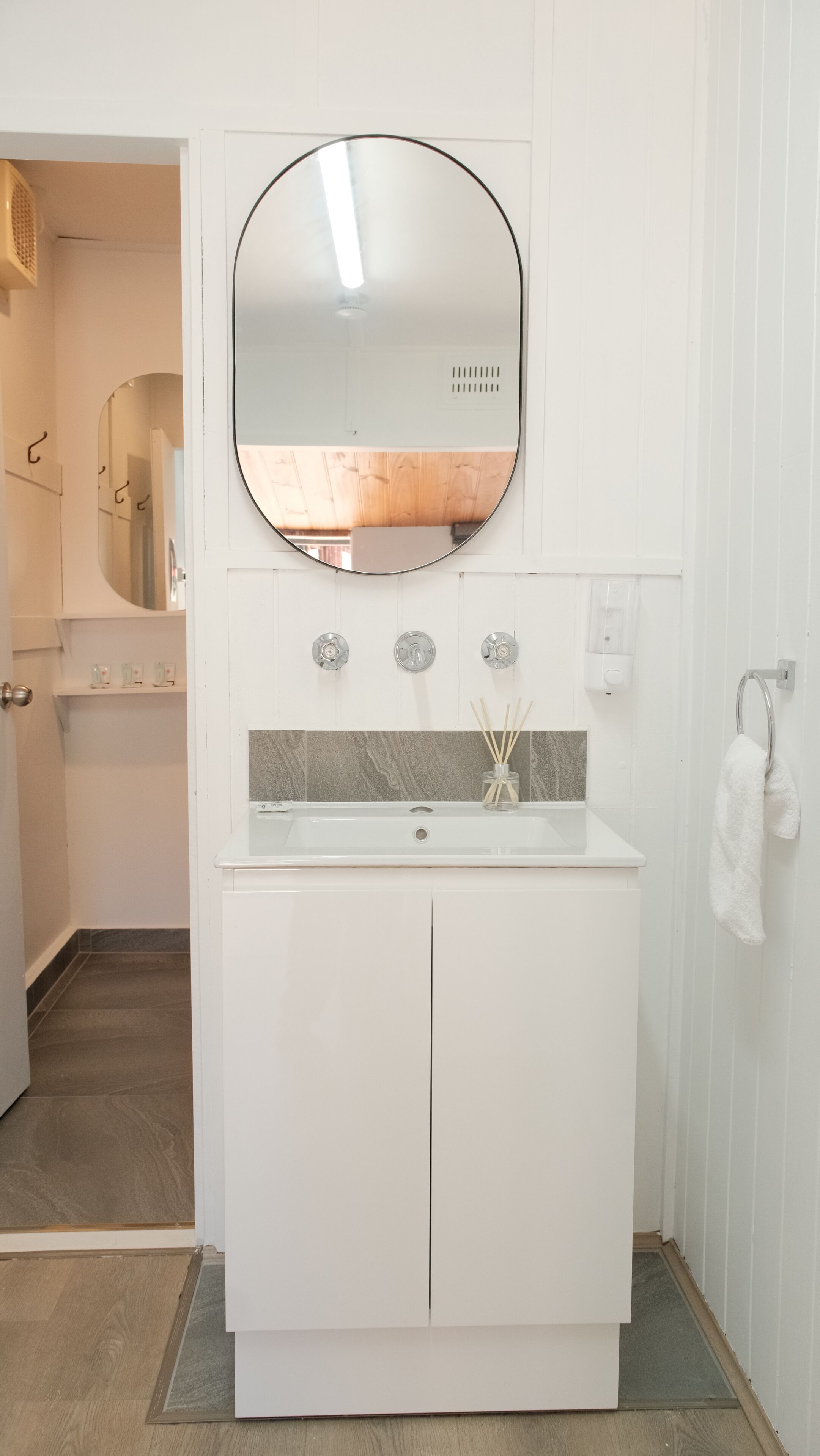 Une salle de bain avec un meuble-lavabo blanc, un miroir rond et un porte-serviettes.