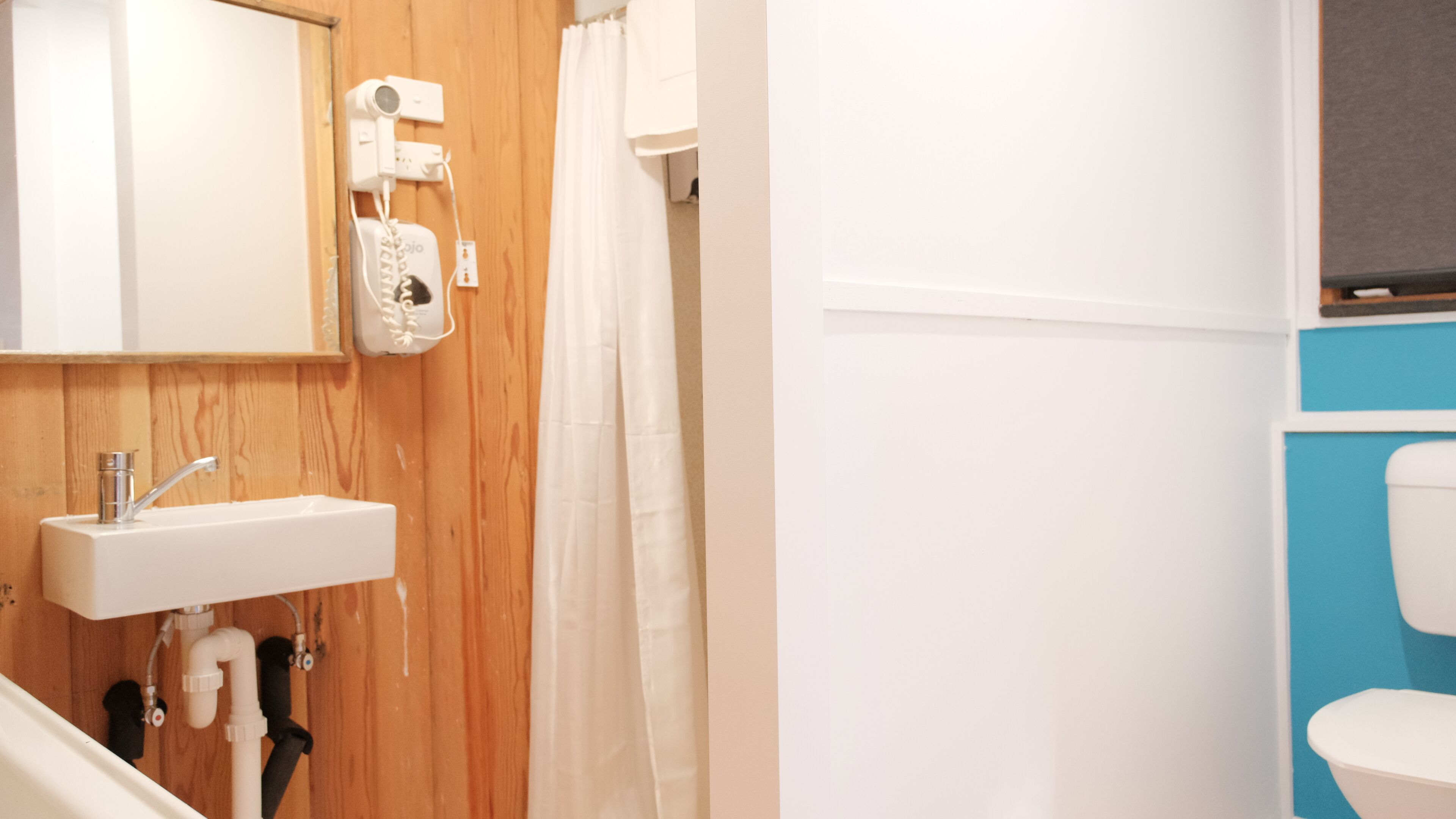 A bathroom with a wooden wall, a white sink, a mirror, a shower curtain, and a toilet.
