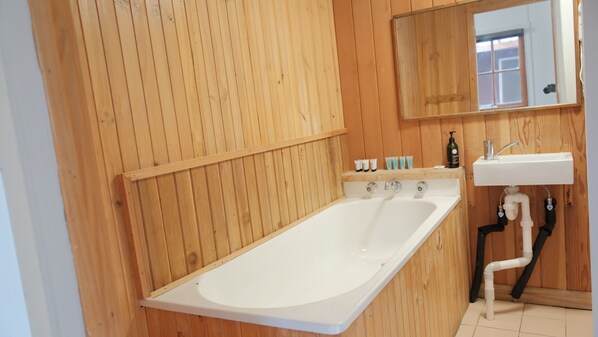 Un baño con paneles de madera, una bañera independiente, un lavabo y un espejo.