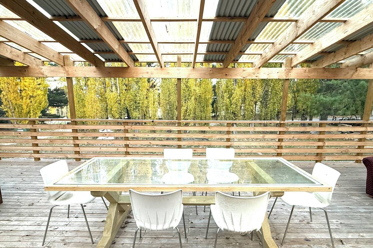 Une terrasse extérieure en bois, dotée d’une table à plateau de verre et de chaises blanches.