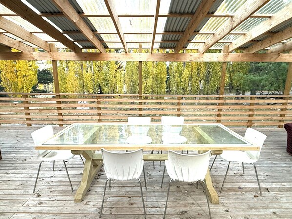 An outdoor wooden deck with a glass-top table and white chairs.