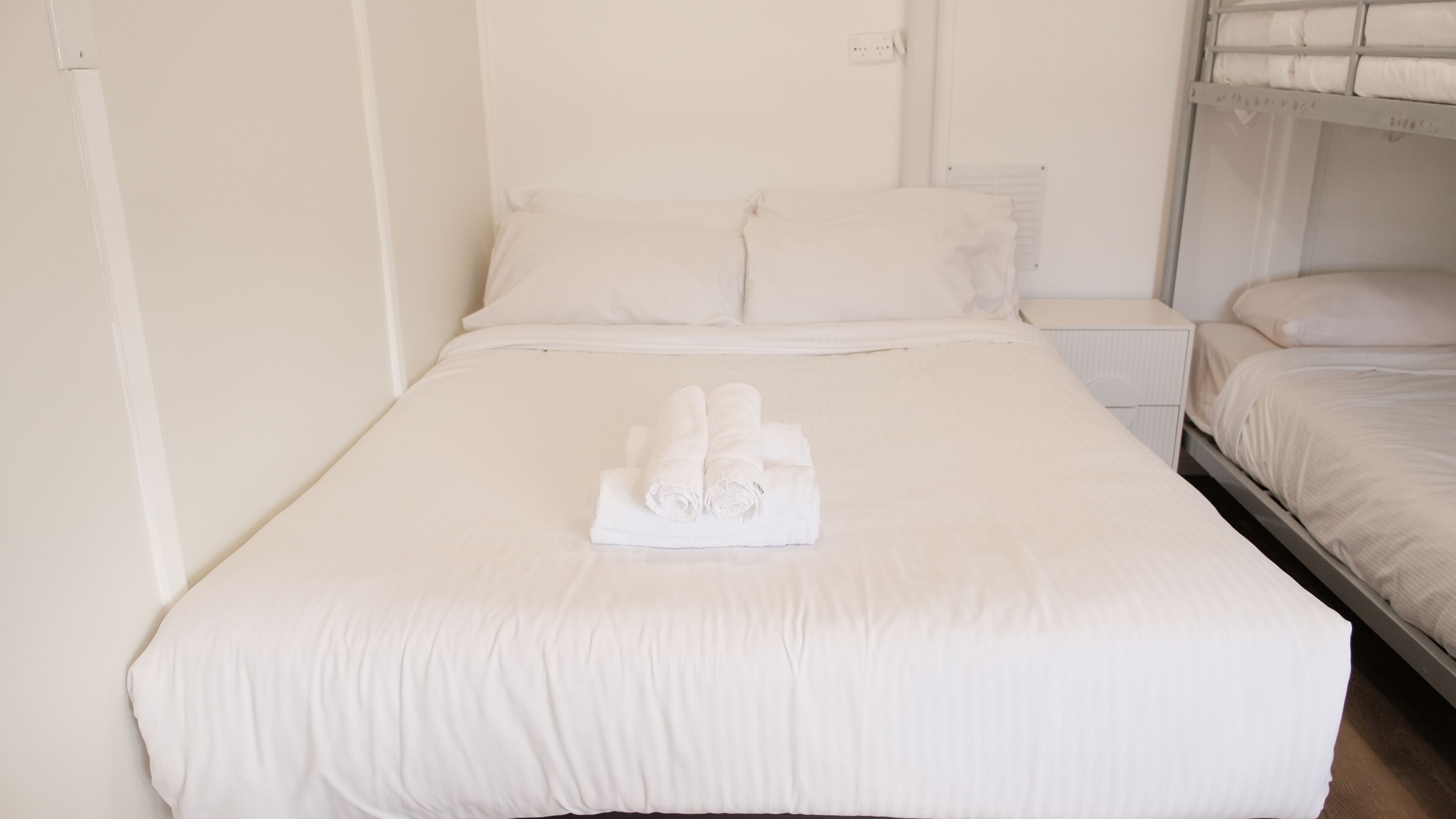A hotel room with a large bed, two bedside tables, and a bunk bed in the corner.