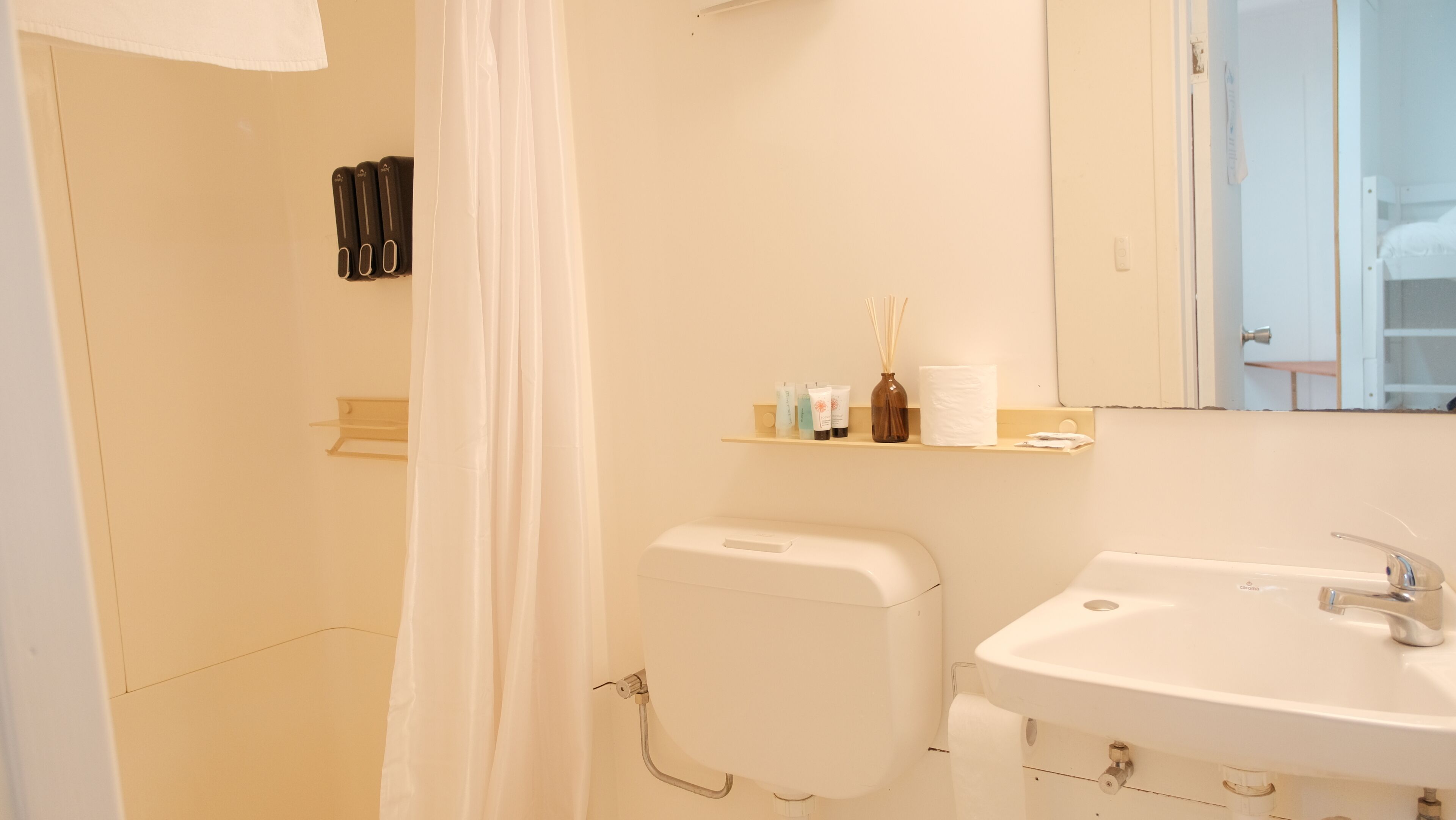 Un baño con cortina de ducha, inodoro, lavabo y un estante con artículos de aseo.