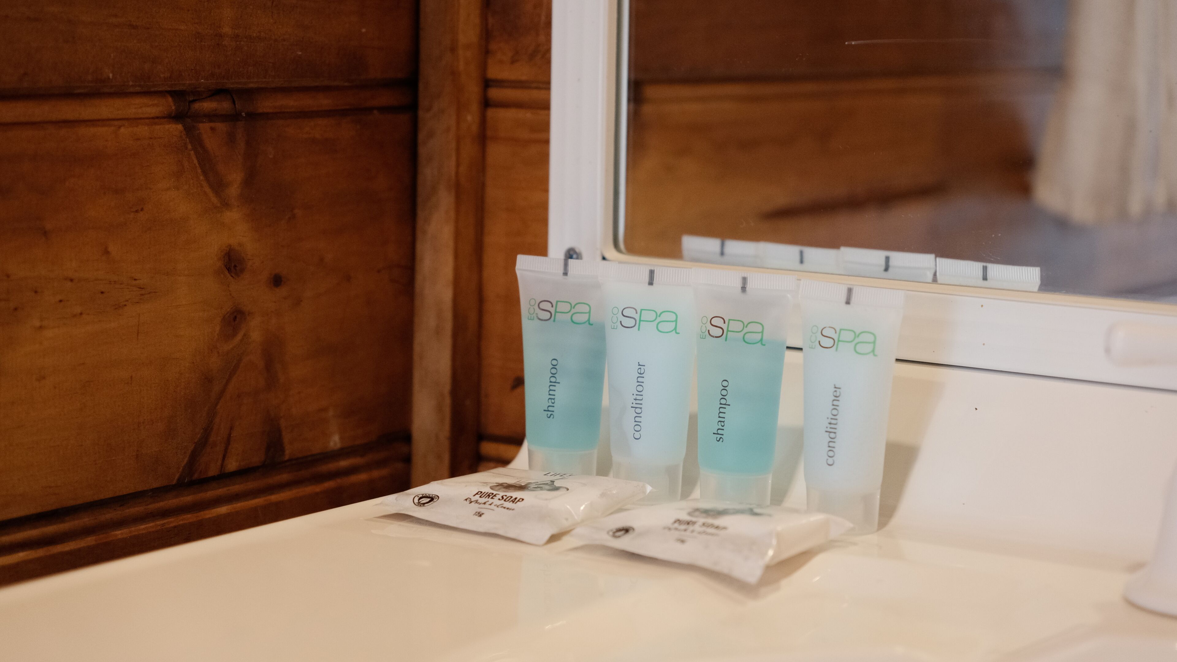 Baño con paneles de madera y una ventana. Hay cuatro botellas de productos de spa sobre el lavamanos.