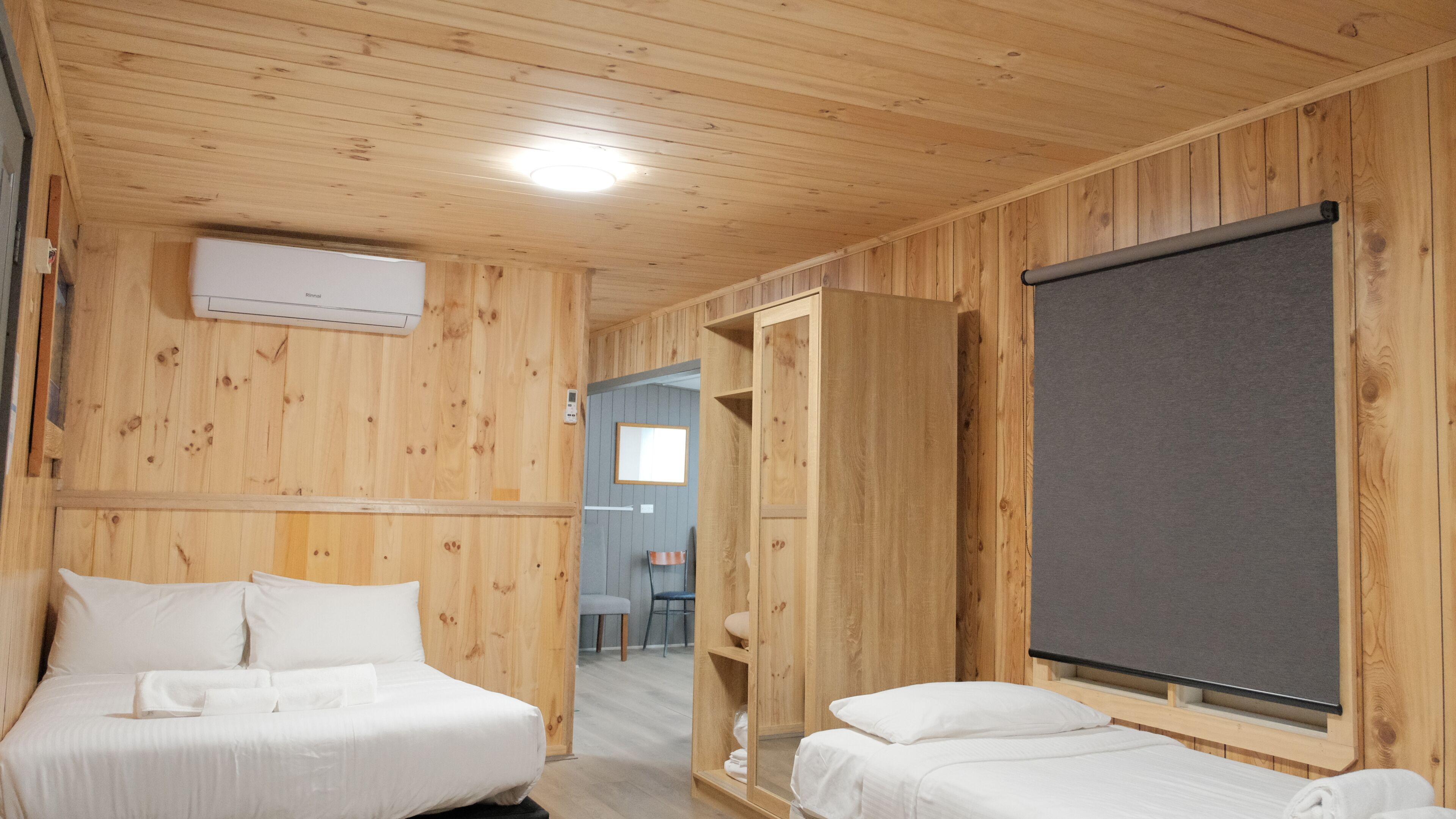 A wooden room with two beds, a large window, and a wall-mounted air conditioner.