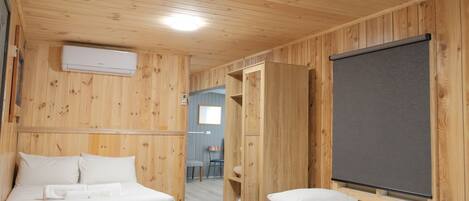 A wooden room with two beds, a large window, and a wall-mounted air conditioner.