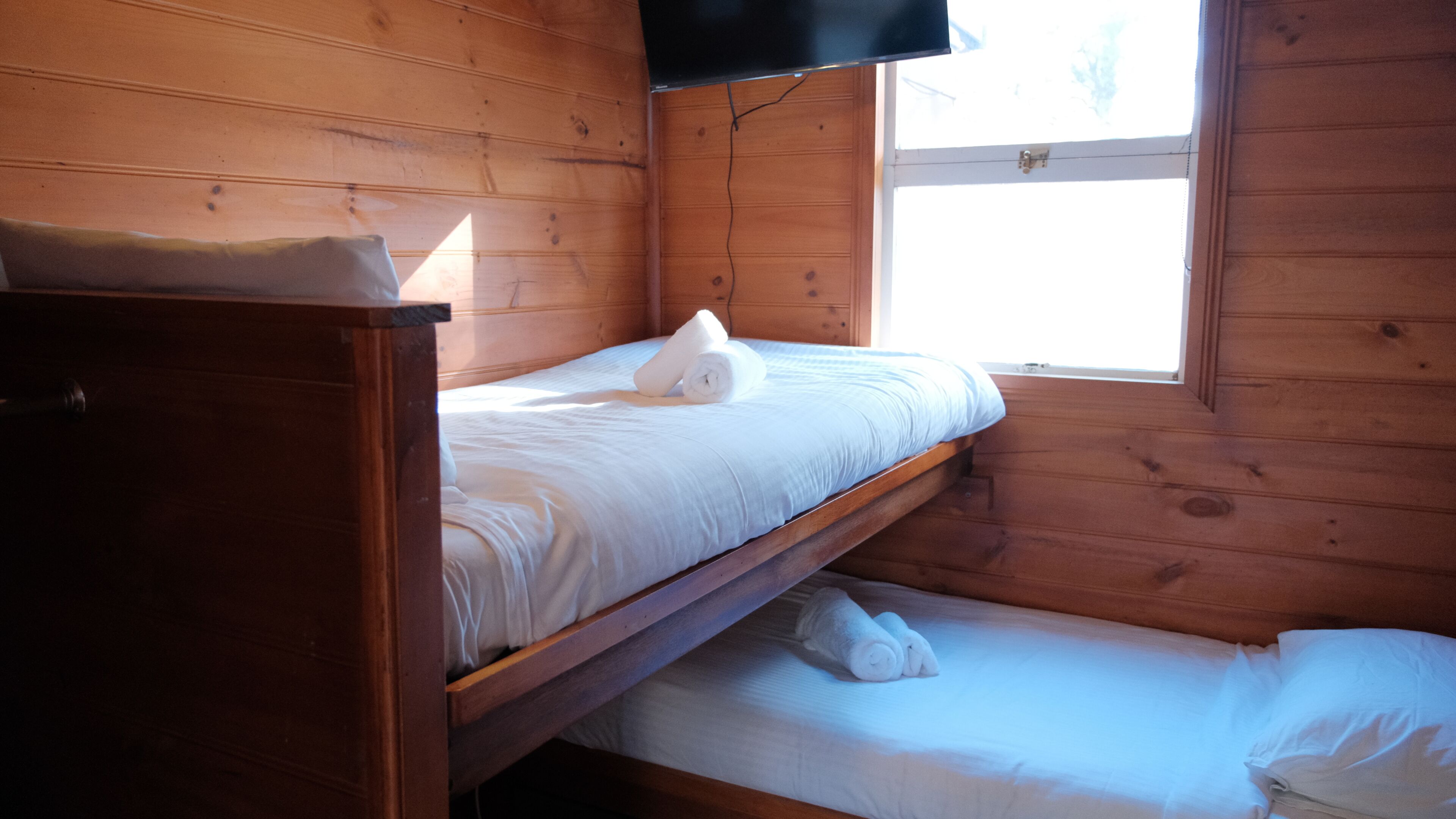 A wooden cabin room with a bunk bed, a small table, and a window.