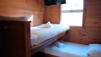 A wooden cabin room with a bunk bed, a small table, and a window.