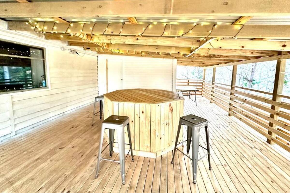Une terrasse en bois avec une table ronde et deux tabourets, une fenêtre et un espace abrité illuminé de guirlandes lumineuses.