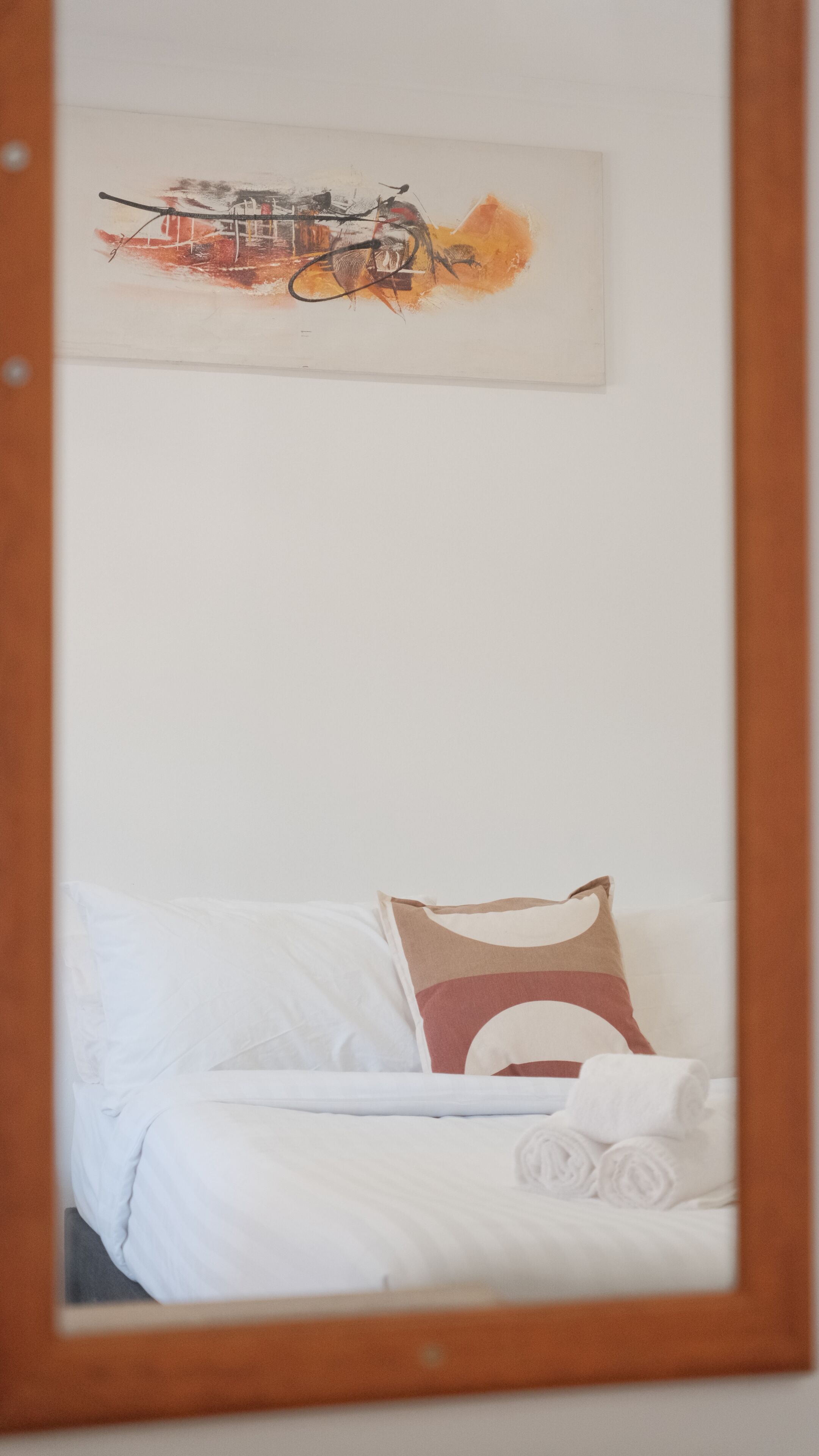 Un dormitorio con cama, almohadas, un cuadro colgado en la pared y un espejo.
