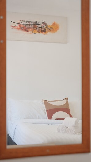 Une chambre à coucher avec un lit, des oreillers, un tableau accroché au mur et un miroir.