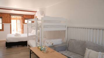 A bunk bed room with a wooden floor, a table with a vase, and a sofa with pillows.