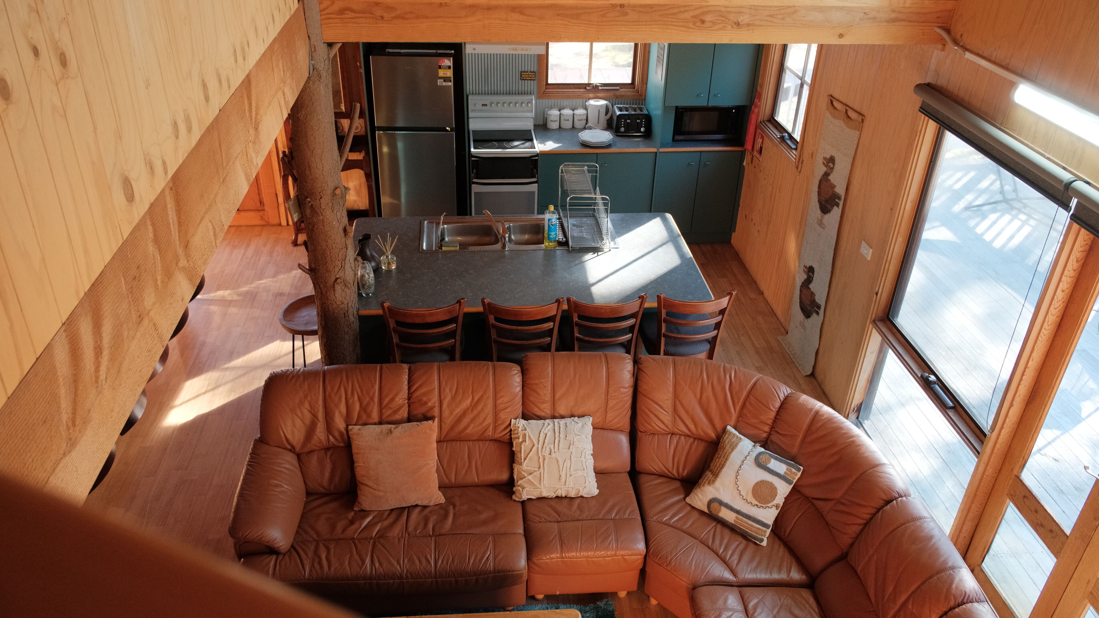 L’intérieur chaleureux d’un chalet comprend un canapé en cuir marron, un coin cuisine avec un réfrigérateur, une cuisinière et des placards, ainsi qu’un coin repas avec des chaises.