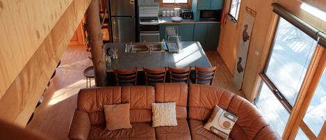 L’intérieur chaleureux d’un chalet comprend un canapé en cuir marron, un coin cuisine avec un réfrigérateur, une cuisinière et des placards, ainsi qu’un coin repas avec des chaises.