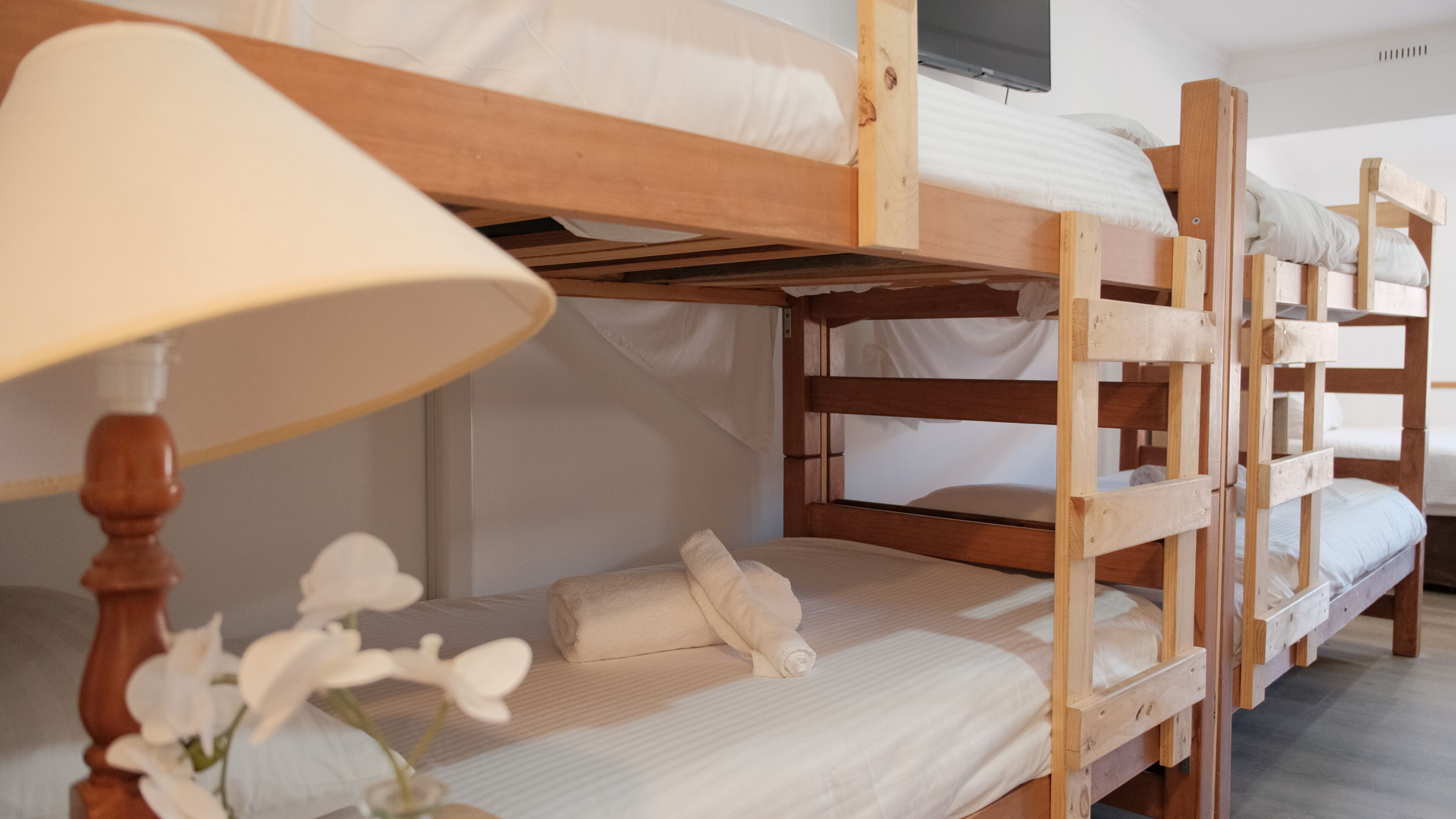 Camas literas con ropa blanca, un cabecero de madera y una lámpara de noche.