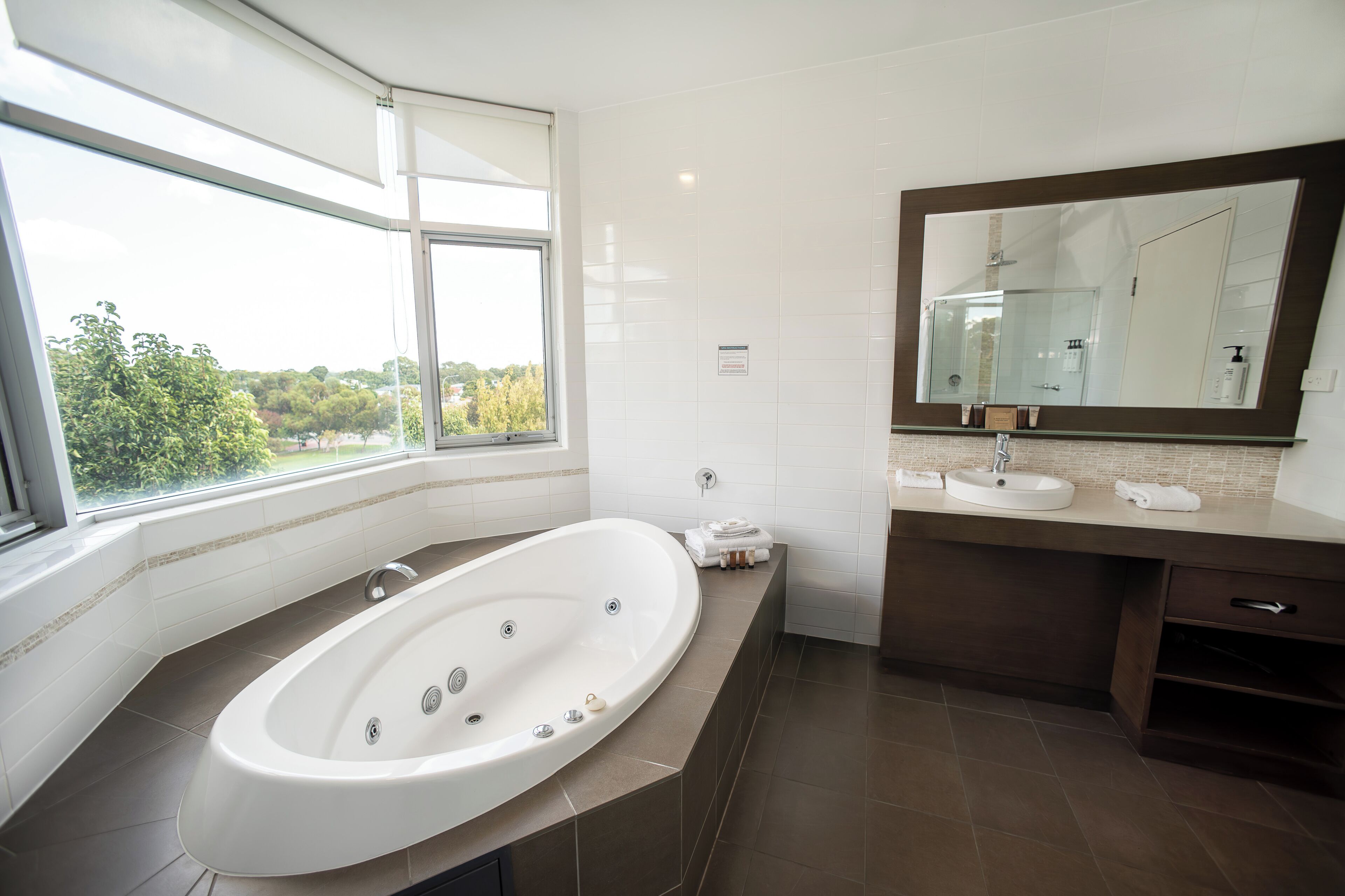 Une salle de bain moderne avec une grande baignoire, un meuble-lavabo avec un miroir et une fenêtre donnant sur la verdure.