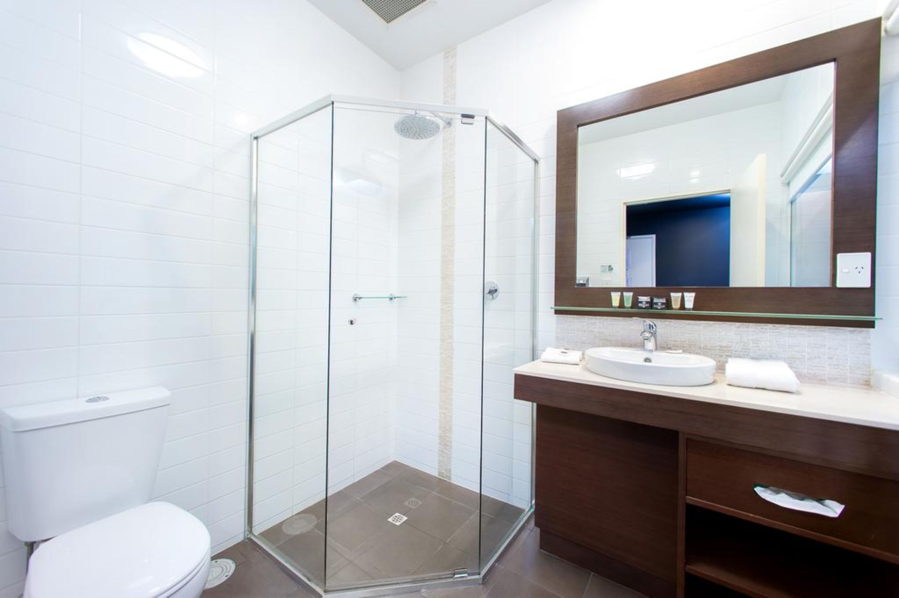 Une salle de bain moderne avec une douche à parois de verre, des toilettes blanches, un lavabo avec un miroir et un meuble-lavabo en bois.