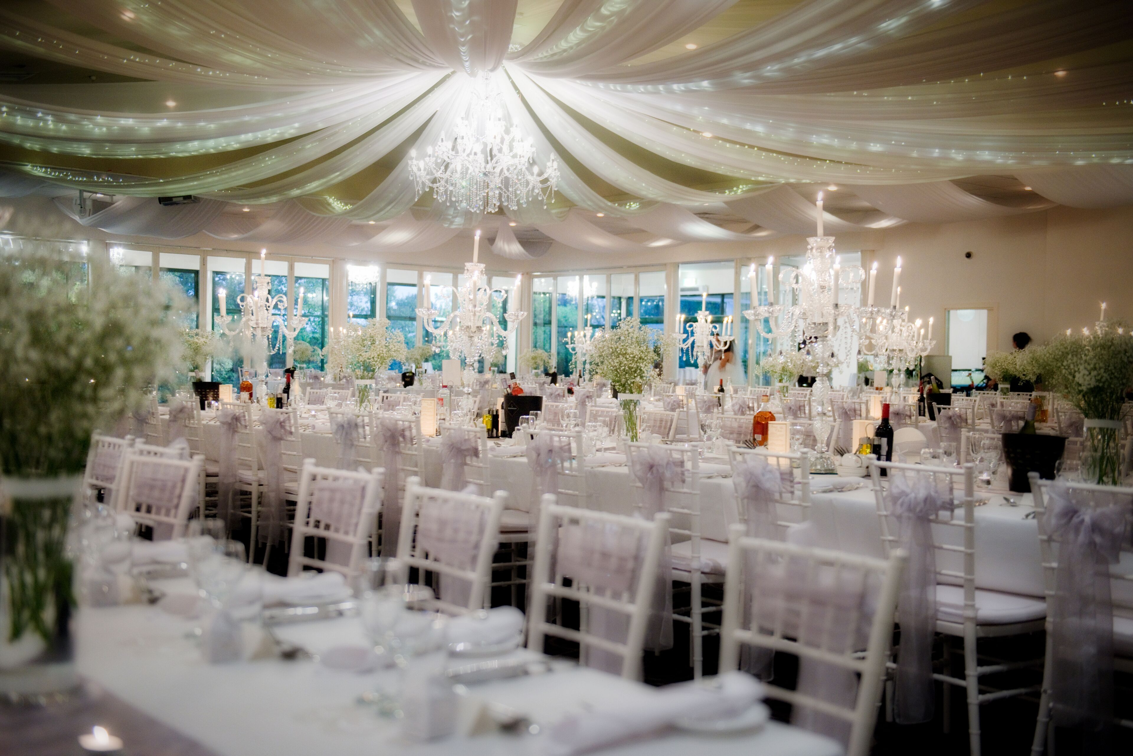 Un salón de banquetes con mesas redondas, sillas blancas y candelabros.