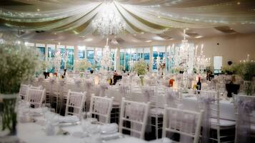 Un salón de banquetes con mesas redondas, sillas blancas y candelabros.
