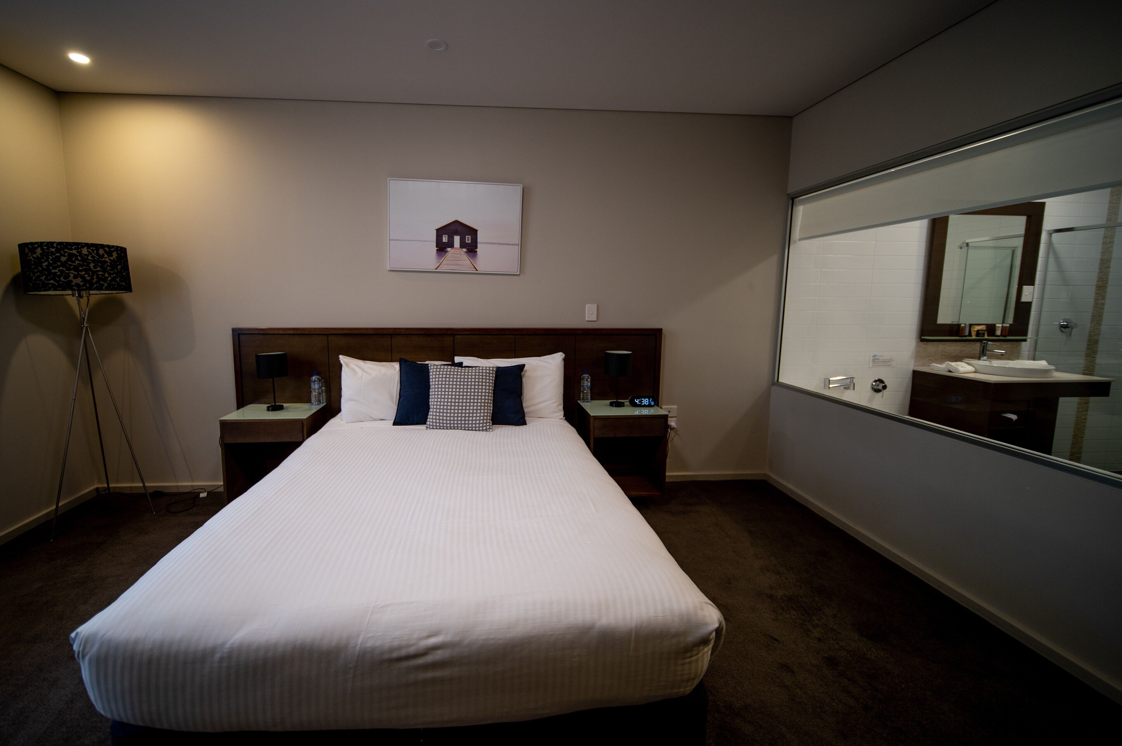 A hotel room with a large bed, two bedside tables, a nightstand, a lamp, a framed picture on the wall, and a large mirror.